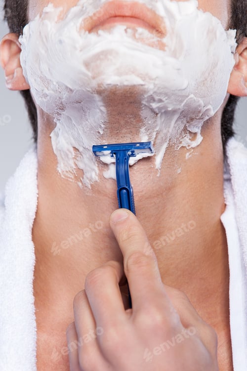 Preview: Close up of shaving. Close up of young man shaving his face while standing against grey background