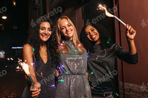 Preview: Three women celebrating new year at night with sparklers and christmas lights