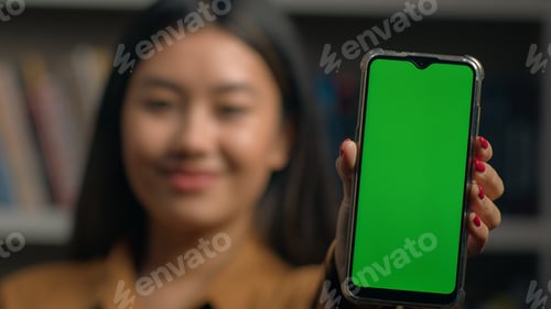 Preview: Smiling asian woman girl holding smartphone showing new application close-up green empty screen