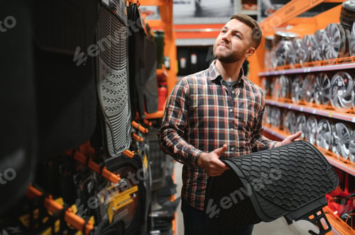 Preview: A man at the car shop or garage choosing floor carpets for his car from given examples
