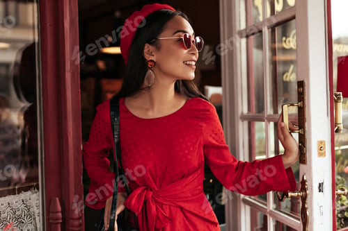 Preview: Tanned charming Asian woman in red dress opens cafe door. Portrait of attractive brunette lady in s