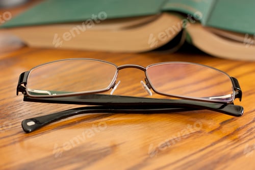 Preview: Eyeglasses and Open Book on Wooden Table