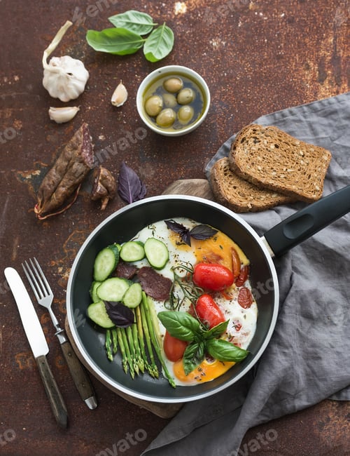Preview: Pan of fried eggs, salami, asparagus, cherry-tomatoes with bread, fresh basil, olives and garlic