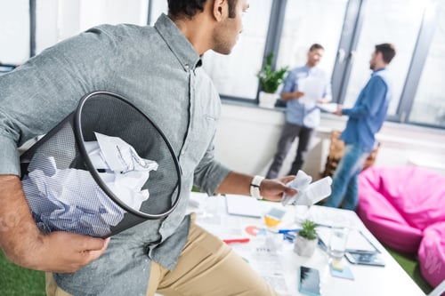 Preview: businessman holding trash bucket with papers and looking at coworkers, business teamwork