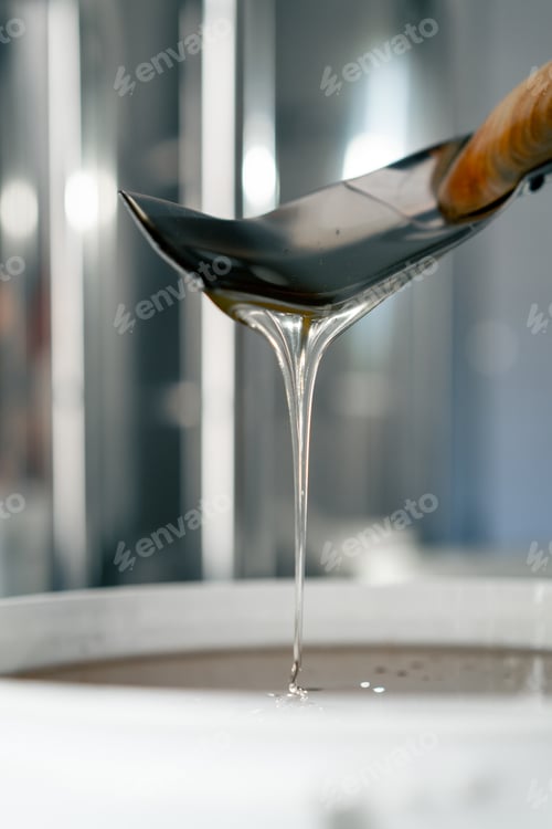 Preview: Close-up shot of a metal spoon stirring natural liquid honey which flows back into large bowl