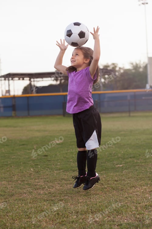 Preview: Girl jumping and heading football on practice pitch