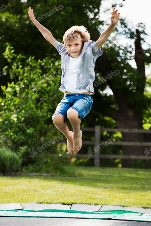 Preview: Boy wearing shirt and denim shorts jumping on a trampoline in a garden.