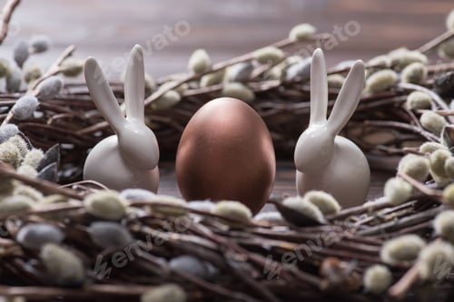 Preview: bronze easter egg and rabbits in catkins nest on table