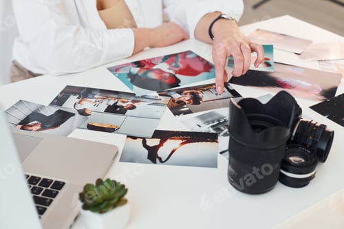 Preview: Close up view of table with camera and photos. Female photographer at work