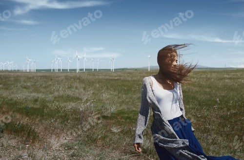 Preview: Woman with long tousled hair next to the wind turbine with the wind blowing