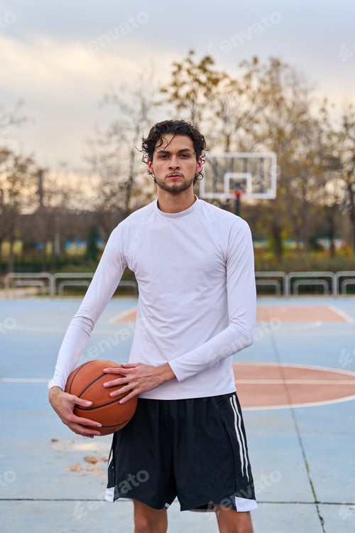 Preview: Young man holding basketball on urban court