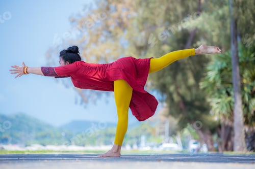 Preview: Asian young healthy woman posing practice bird of paradise yoga on stone beach with blue cloud sky a
