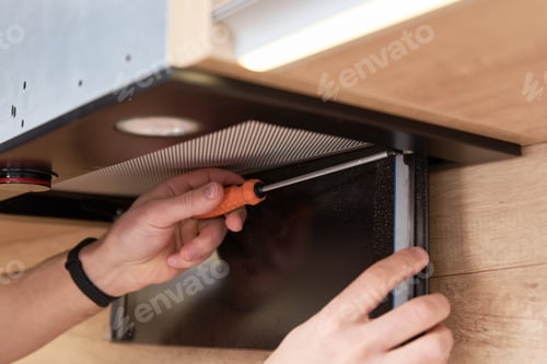 Preview: Man repairs hood in kitchen. Replacement filter in cooker hood