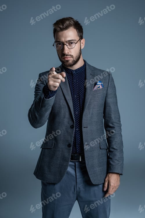 Preview: Young handsome man in formal suit and glasses pointing finger at camera