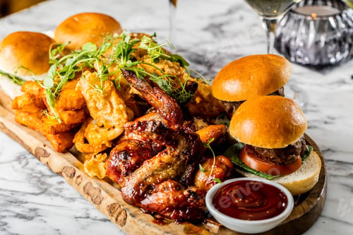 Preview: Closeup shot of a wooden plate with burgers, fried chicken wings with a bowl of ketchup
