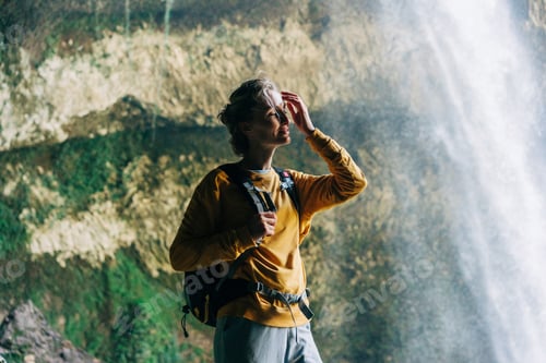 Preview: Portrait of an active woman hiker with a backpack in a mountain canyon near a large waterfall.