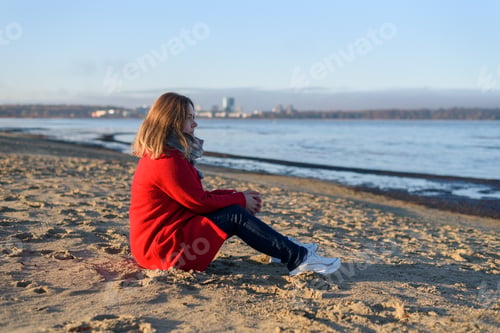 Preview: Woman in red coat sitting near sea