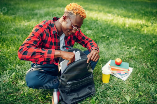Preview: Black student with backpack sitting on the grass