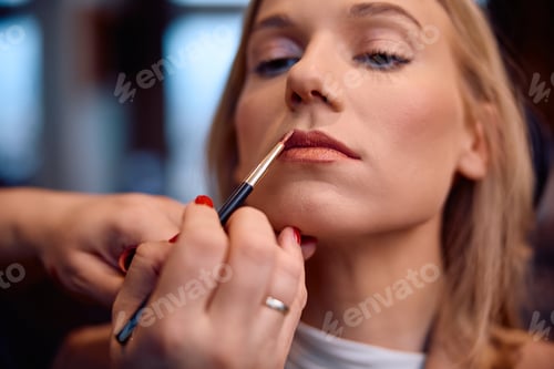 Preview: Close up of make-up artist applying color on woman's lips.