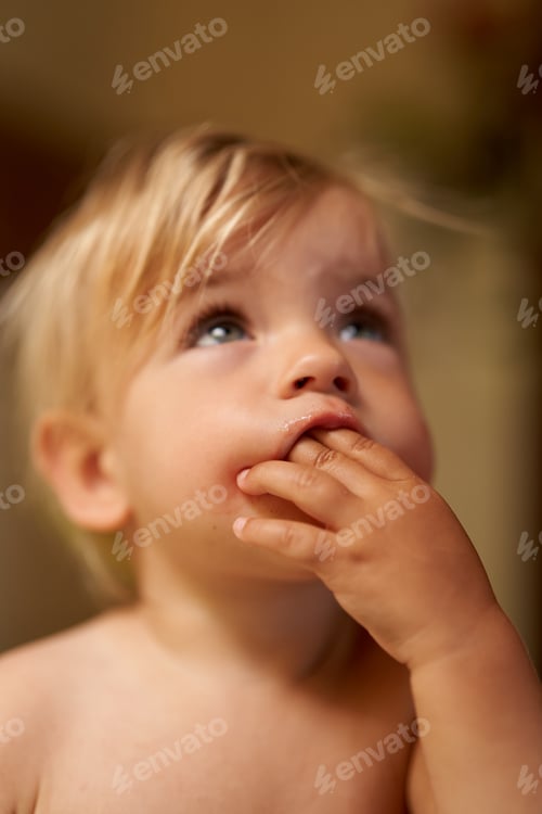 Preview: Small child with a hand in his mouth looks up. Portrait