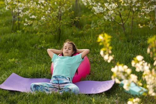 Preview: little girl in a T-shirt does yoga on a mat in the garden. a child and a healthy lifestyle