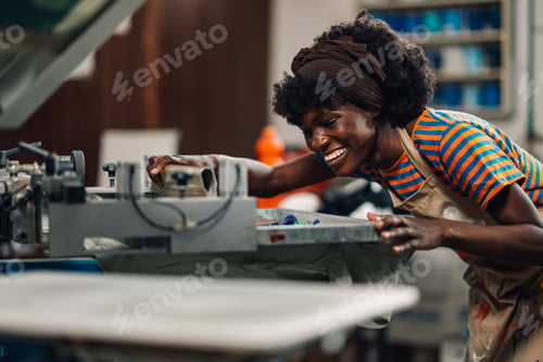 Preview: Happy interracial printing shop worker screen printing with squeegee.