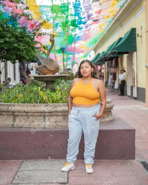 Preview: Street portrait of young woman looking at camera with multicolored flags in background.