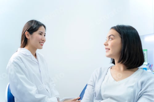 Preview: Caucasian beautiful girl talks and consult with Asian female dentist for cavities and gum disease