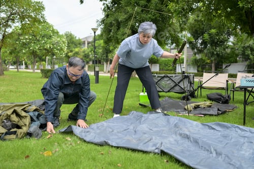 Preview: Senior man and woman setting up a camping tent together in a park