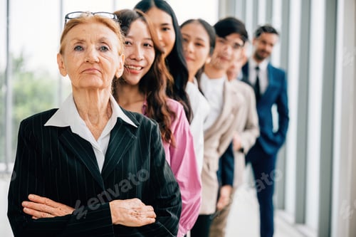 Preview: Young businesspeople, along with a senior woman, confidently gather indoors, standing with crossed