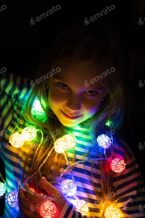 Preview: portrait of a girl holding in hand a garland, glowing with colorful multicolored lights at night