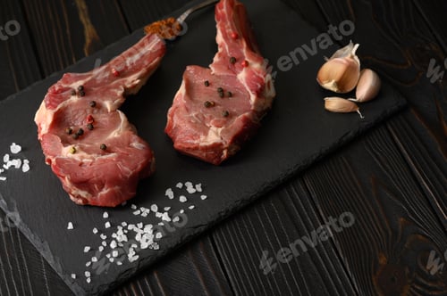 Preview: Raw cowboy steak and spices on a black wooden background.