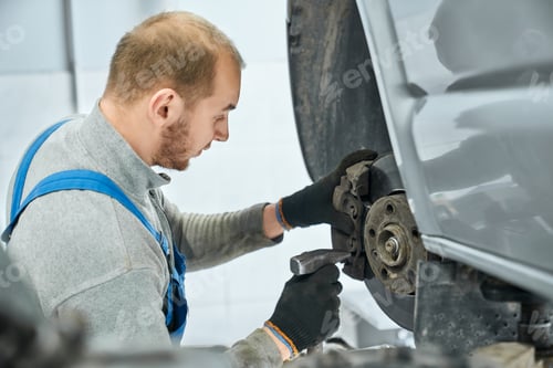 Preview: Mechanic checking serviceability of brake pads in lifted car