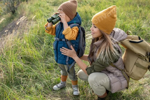 Preview: Young female backpacker in warm casualwear squatting by her adorable little son