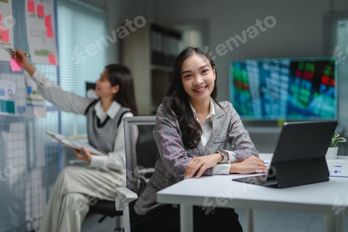 Preview: Businesswoman smiling and working with tablet while colleague analyzing financial charts