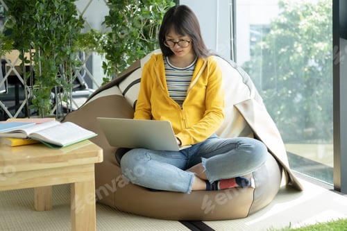 Preview: Beautiful young woman sitting on couch working on laptop.