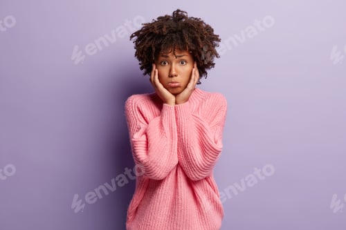 Preview: Sad dejected African American woman touches cheeks with both hands, has miserable facial expression,