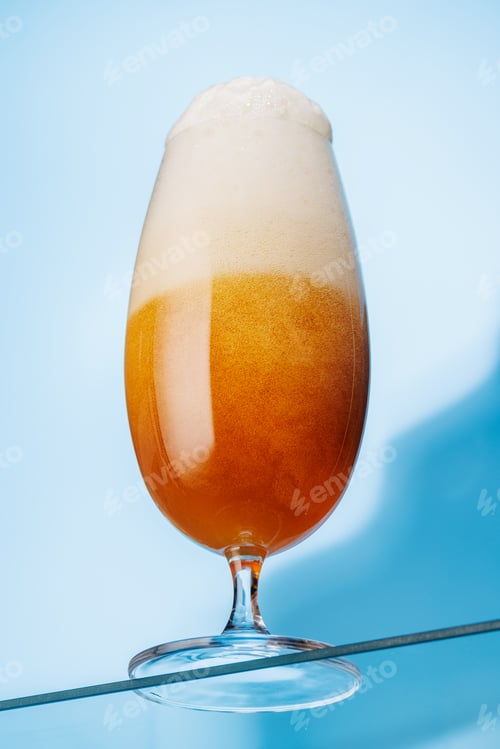 Preview: A tall glass of beer with a golden hue and frothy head, on a blue background