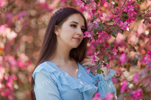 Preview: girl is standing near a pink blooming apple tree