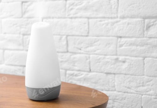 Preview: Essential oils diffuser on wooden table near brick wall. Space for text