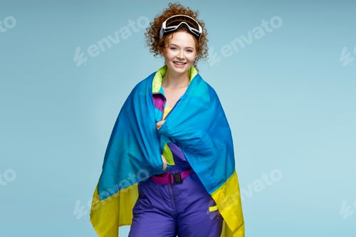 Preview: Smiling sportswoman wearing ski goggles and wrapped in ukrainian flag