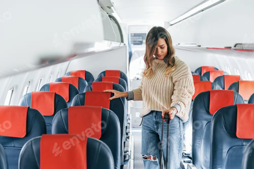 Preview: Holding lugagge. Young female passanger in casual clothes is in the plane