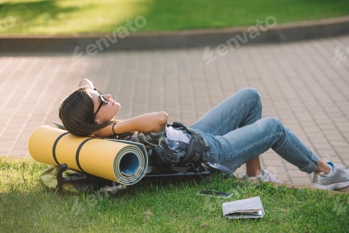 Preview: young woman in sunglasses lying with backpack on grass