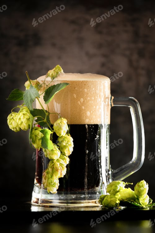 Preview: Glass of dark beer with hops around on a dark background