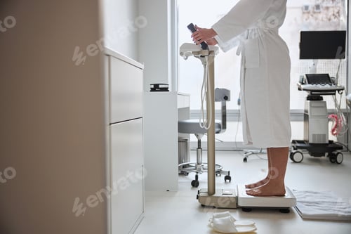 Preview: Barefoot Caucasian lady in a bathrobe measuring her body weight