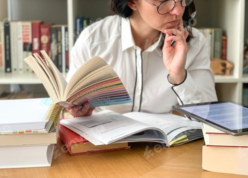 Preview: Back to school: young millennial female student is studying from home. Pile of books and tablet