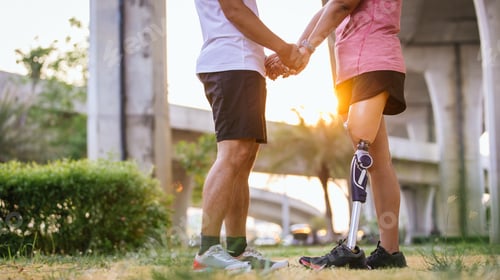 Preview: Couple holding hands in the park. Woman has bionic prosthetic Leg . Reaching for each other.