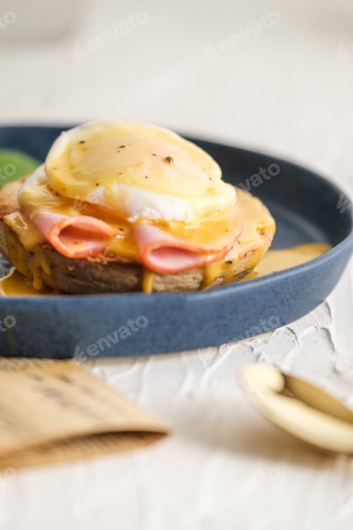 Preview: egg Benedict with hollandaise sauce on blue plate on table in white kitchen