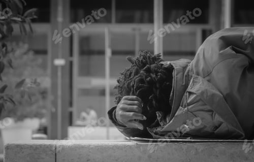 Preview: Grayscale shot of an African-American person wearing a coat and lying on a bench outdoors