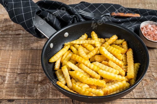 Preview: Fried Crinkle oven French fries potatoes sticks in a pan. Wooden background. Top view